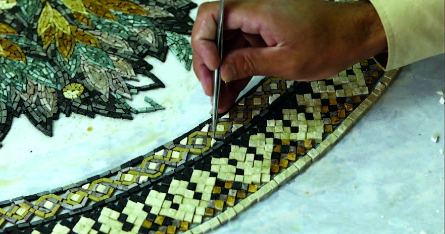 An artisan placing stones along a mosaic border with tweezers