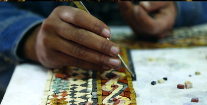 Hands setting small stones into a mosaic pattern